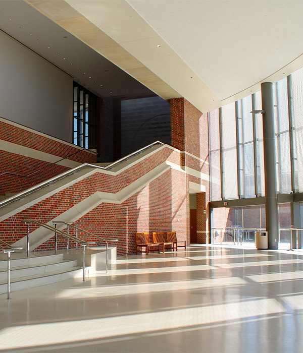 Sunlit modern building lobby with brick staircases and large floor-to-ceiling windows along one wall.
